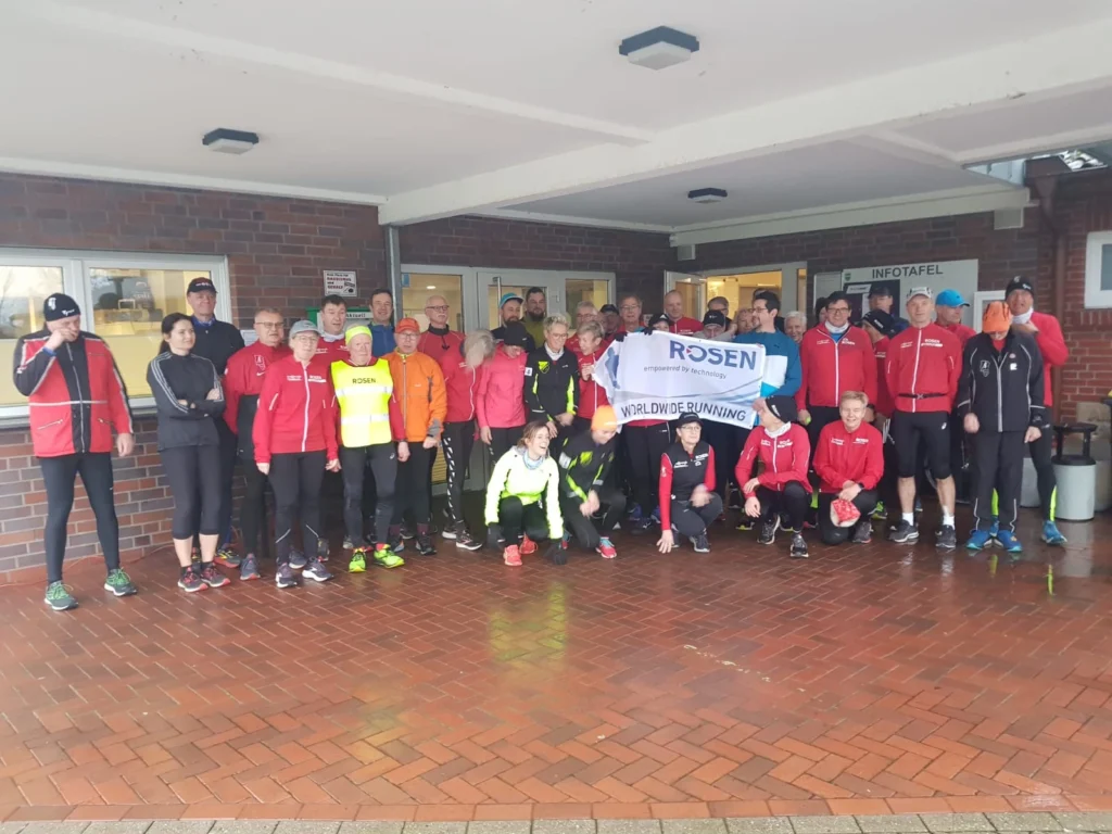 Gruppe von Läufern in Sportkleidung posiert mit einem Banner vor einem Gebäude für ein gemeinsames Lauf-Event.
