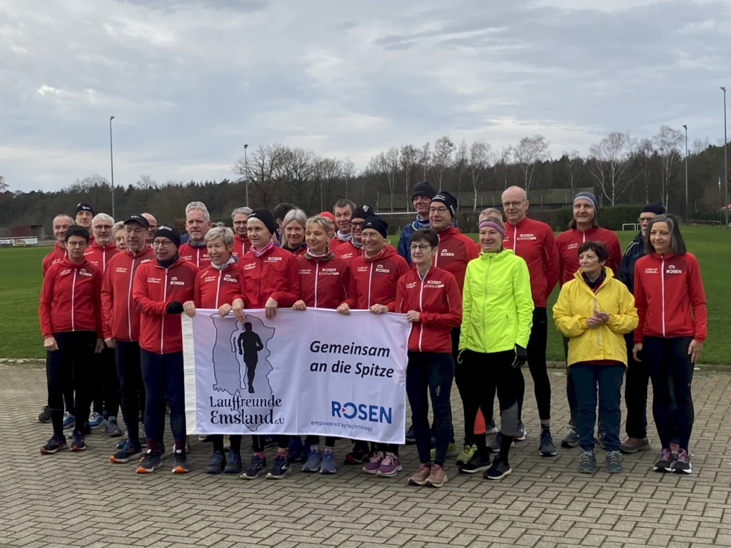 Gruppe von Läufern in roten Jacken hält ein Banner mit dem Logo der Lauffreunde Emsland und dem Slogan Gemeinsam an die Spitze.