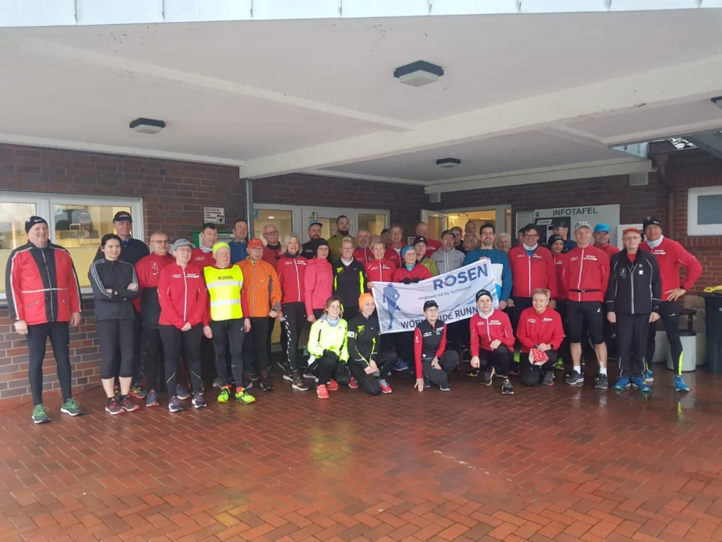 Gruppe von Läufern in Sportkleidung mit Banner, posierend vor einem Gebäude bei Regenwetter.