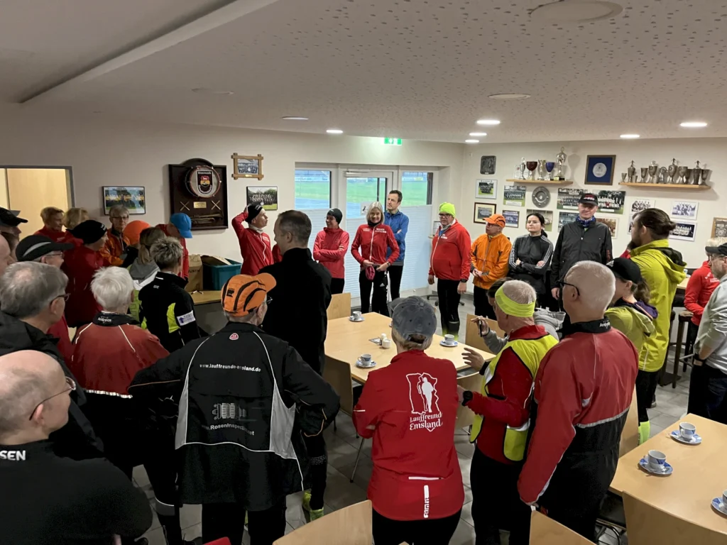 Eine Gruppe von Menschen in Sportbekleidung versammelt sich in einem Raum, umgeben von Trophäen und Bildern an der Wand.