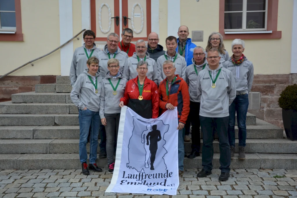 Gruppe von Läufern mit Medaillen und Vereinsbanner Lauffreunde Emsland posiert auf Treppen vor historischem Gebäude.