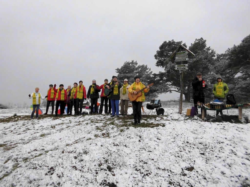 Gruppe singt und spielt Gitarre im verschneiten Park, Wegweiser zeigt Richtung, winterlicher Ausflug mit Musik.