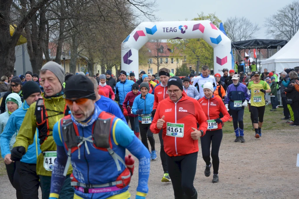 Läufergruppe beim Start eines Marathons im Freien, umgeben von Herbstbäumen und Zuschauern bei kühlem Wetter.
