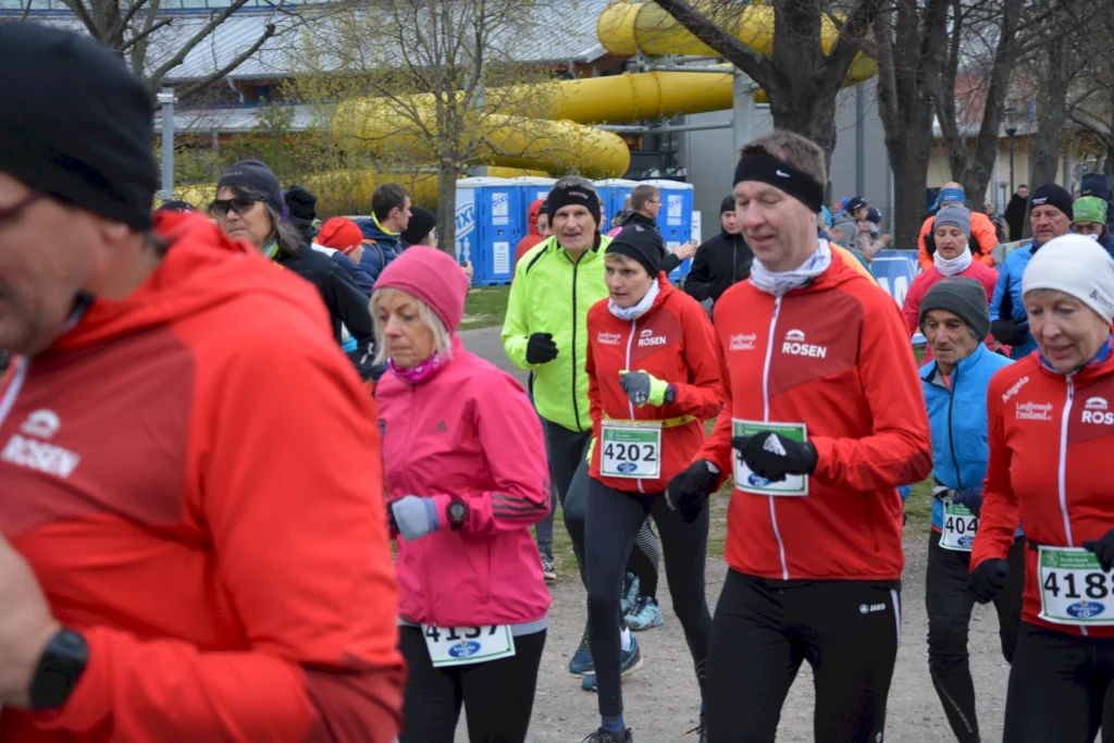 Läufer in bunter Sportkleidung bei Herbstlauf auf Waldweg, umgeben von Bäumen und Zuschauern.