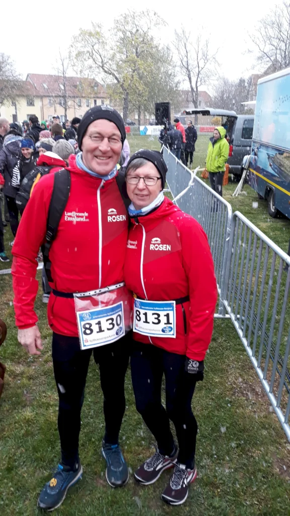 Teilnehmer eines Winterlaufs posieren lächelnd im Zielbereich, gekleidet in rote Jacken mit Startnummern 8130 und 8131.