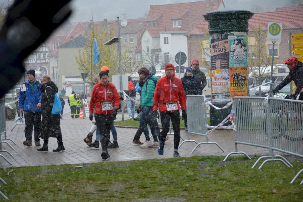Marathonläufer in roter Kleidung bei Schneefall in einer Stadt, umgeben von Zuschauern und Werbeplakaten.