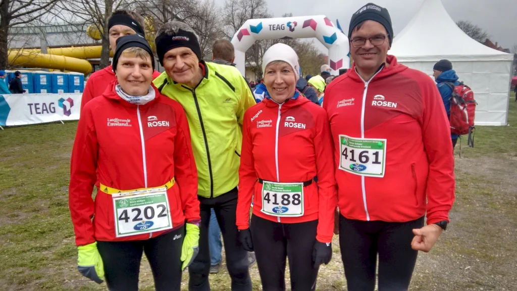 Läuferteam in roten Jacken beim Wettkampfstart, mit Startnummern und TEAG-Banner im Hintergrund. Wetter bewölkt.