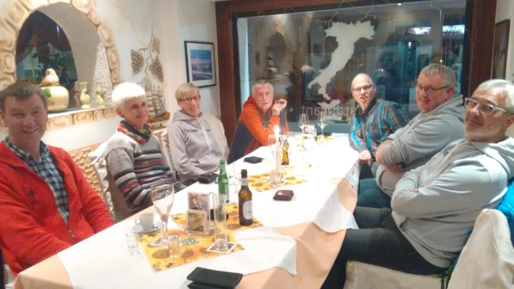 Gruppe von acht Personen am Tisch in gemütlichem Restaurantambiente, lächelnd und mit Getränken, fröhliche Runde.