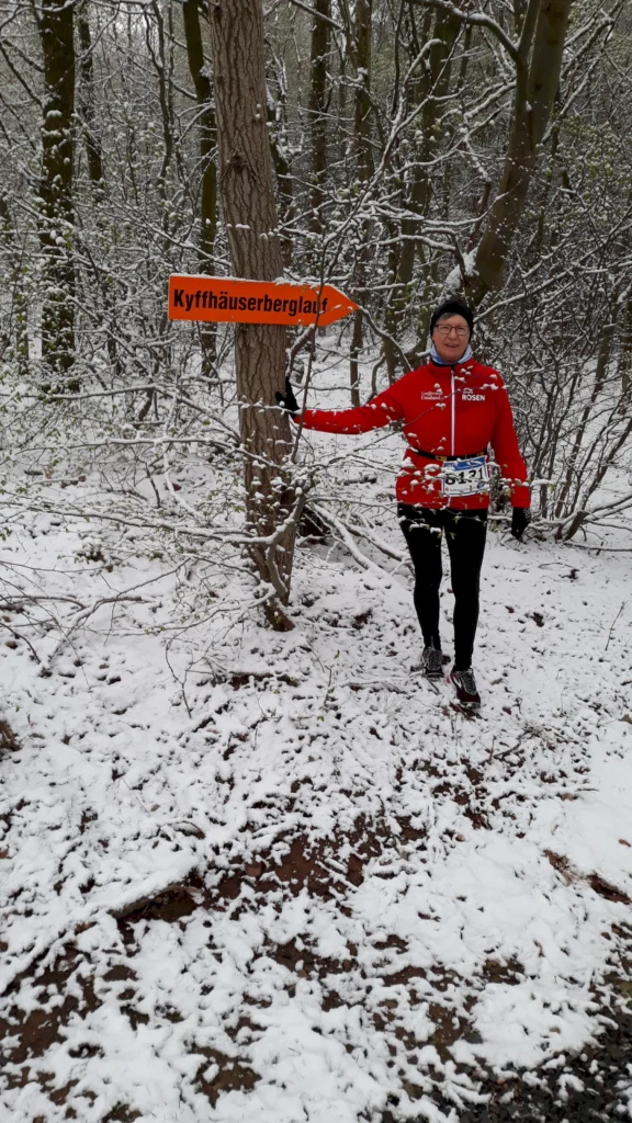 Läufer bei Kyffhäuserberglauf im schneebedeckten Wald mit Hinweisschild, rote Jacke und Startnummer.