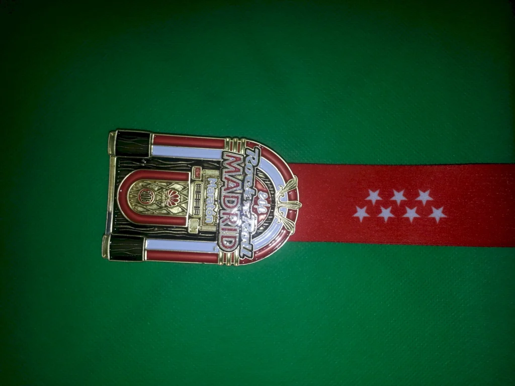 Medaille des Rock 'n' Roll Marathons in Madrid 2016, mit rotem Band und goldener Auszeichnung, auf grünem Hintergrund.