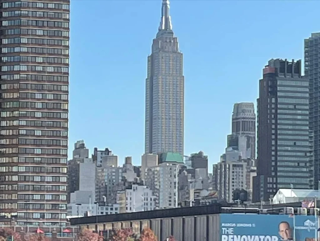 Blick auf das Empire State Building in New York City, umgeben von modernen Wolkenkratzern und einem blauen Himmel.