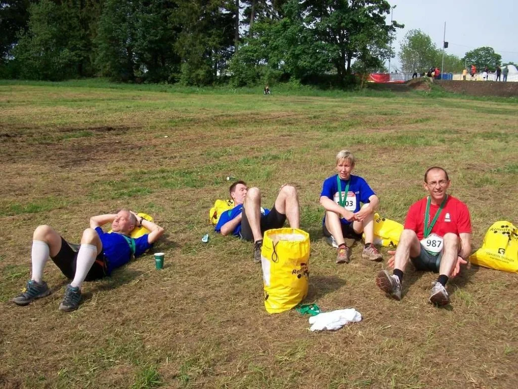 Vier Läufer erholen sich nach einem Rennen auf einer Wiese mit gelben Taschen und Medaillen um den Hals.