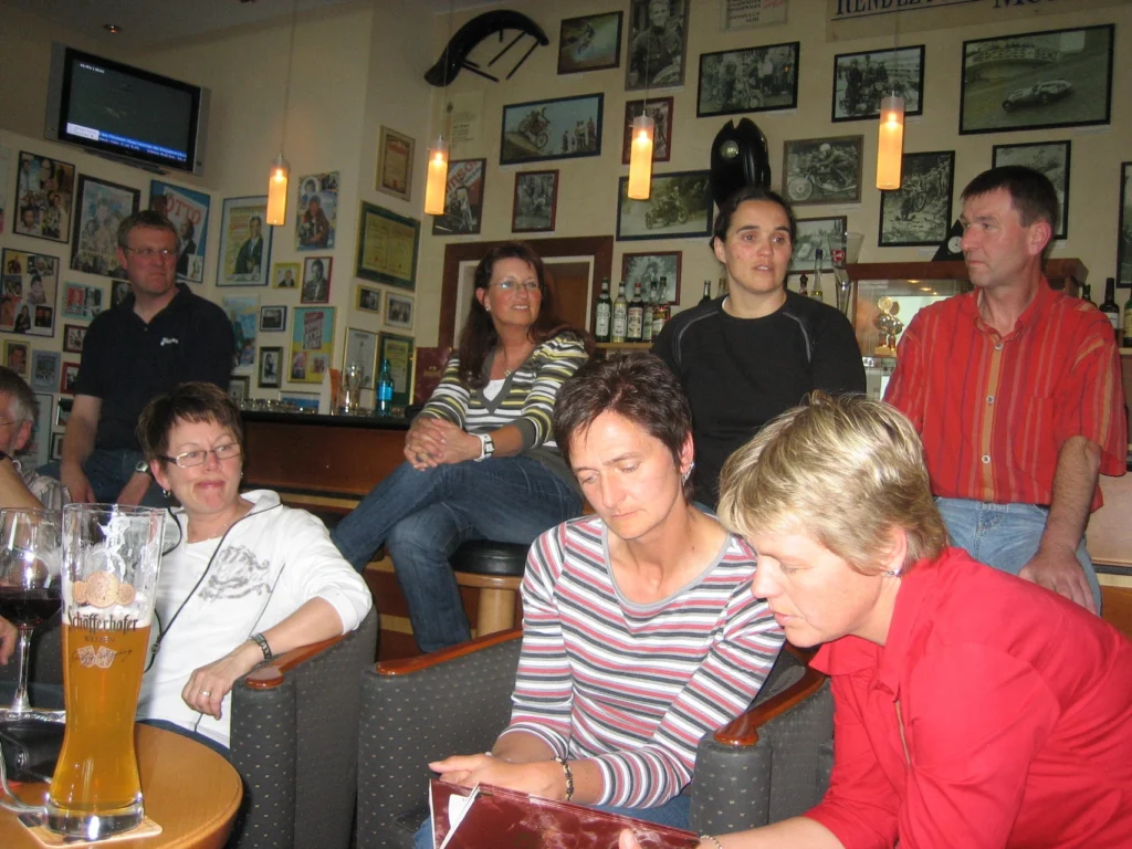 Gruppe von Menschen in einer gemütlichen Bar, einige sitzen an der Theke und andere lesen ein Menü.