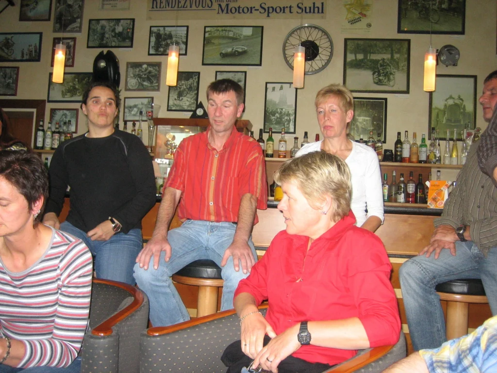 Gruppe von Menschen in einer Bar mit dekorativen Motorradbildern im Hintergrund, entspannte Stimmung.