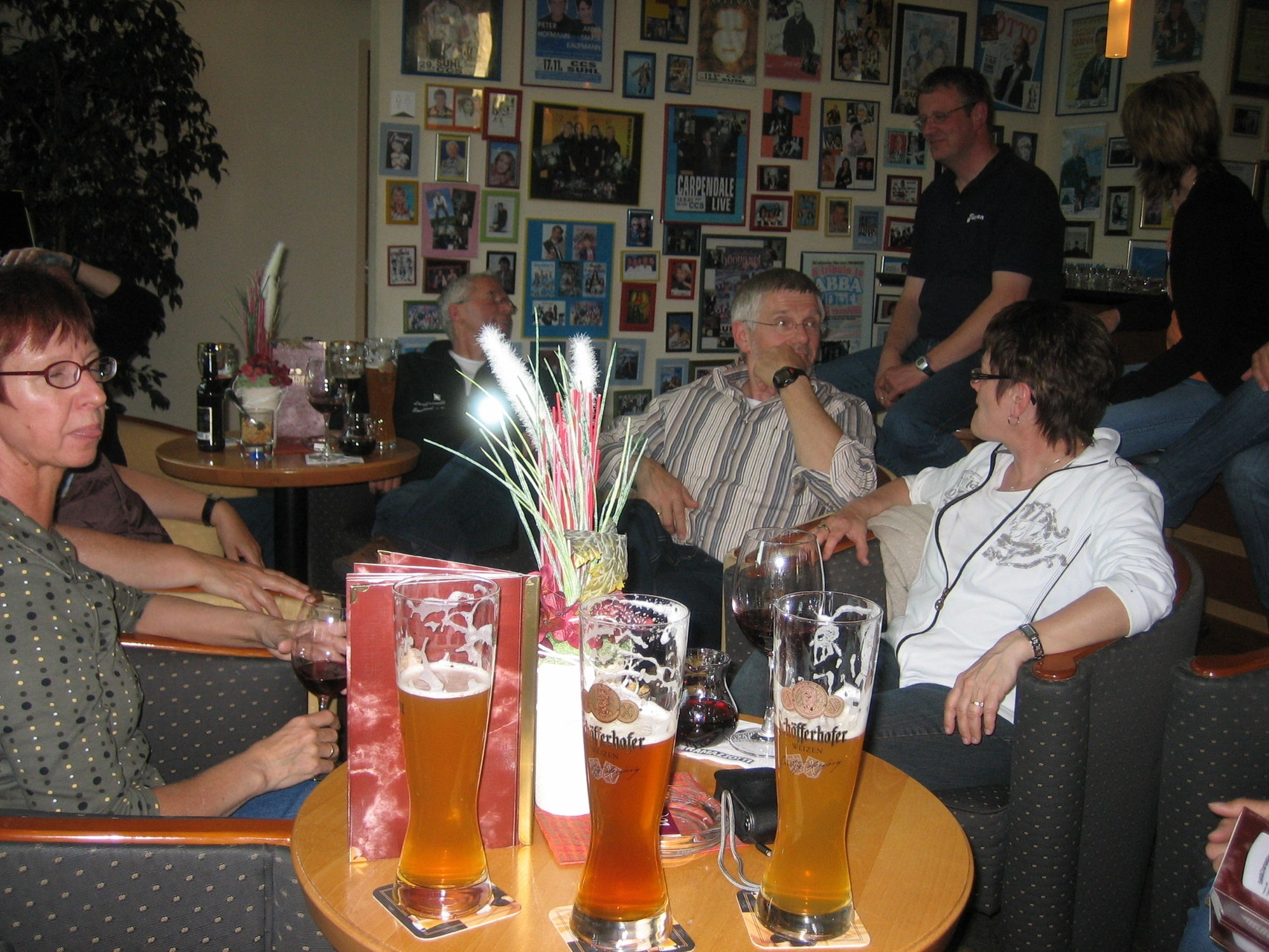Gruppe von Menschen entspannt in einer Bar, mit Getränken und Bildern an der Wand im Hintergrund.