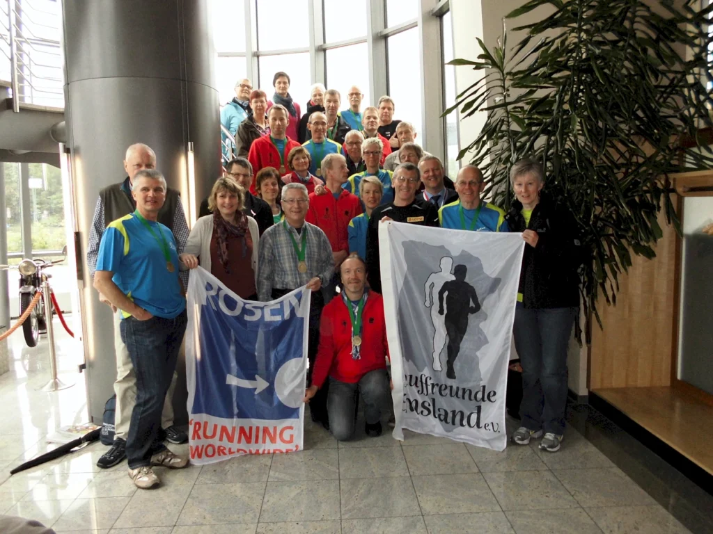 Gruppe von Menschen posiert in einem Gebäude mit Fahnen, die Laufen symbolisieren. Running-Community-Treffen.