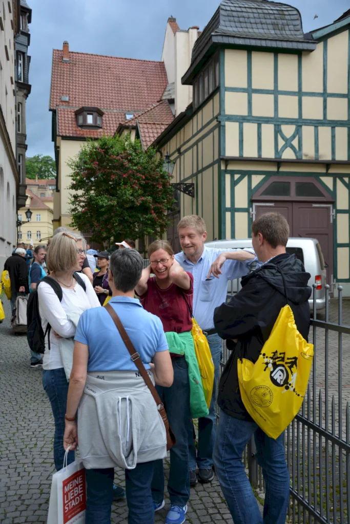 Gruppe lachender Menschen in historischem Stadthintergrund mit Fachwerkhaus und sommerlicher Atmosphäre.