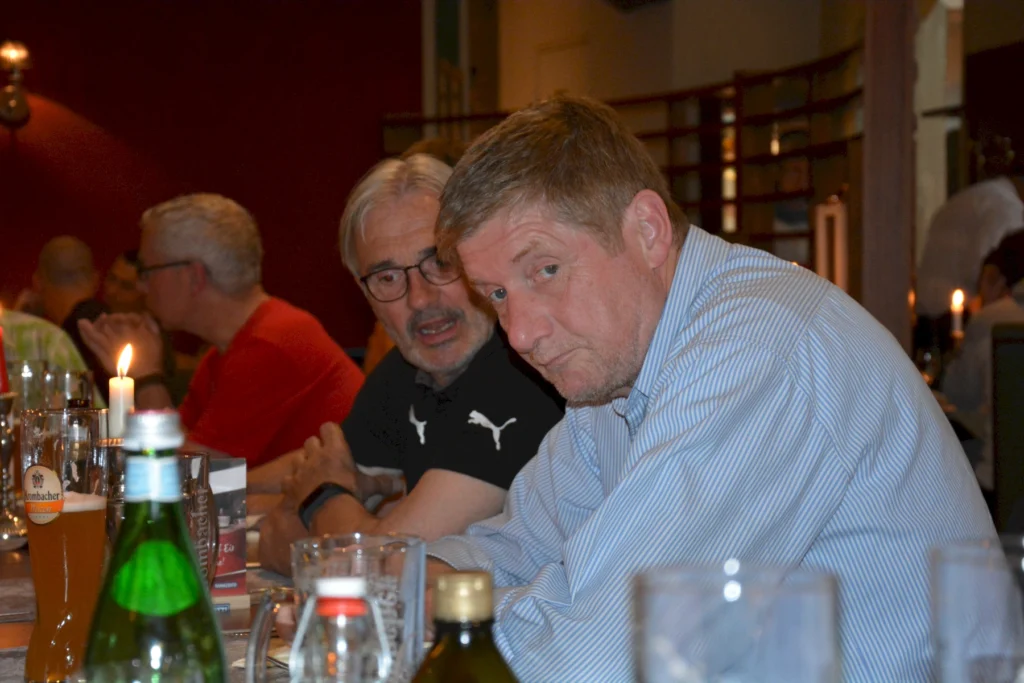 Männer unterhalten sich in einem gemütlichen Restaurant bei Kerzenschein, mit Wasserflasche und Bier auf dem Tisch.