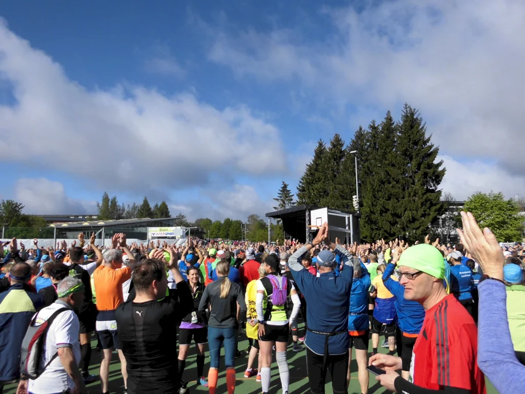 Teilnehmer wärmen sich auf vor einem Laufmarathon im Freien, bei sonnigem Wetter unter blauem Himmel mit Wolken.