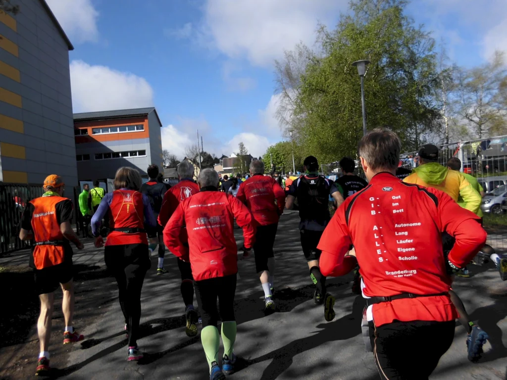 Teilnehmer laufen bei einem sonnigen Marathon in bunter Sportkleidung. Gebäude und Bäume im Hintergrund.