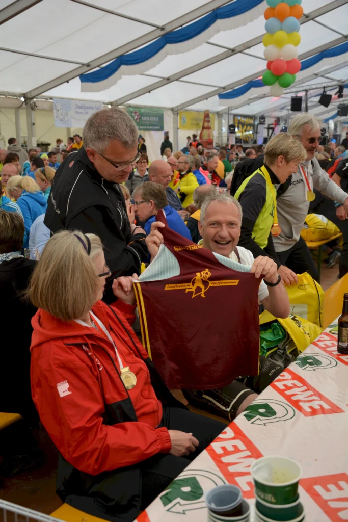 Personen genießen ein Festzelt-Event, halten gemeinsam ein Trikot und lächeln. Fröhliche Gemeinschaftsveranstaltung.