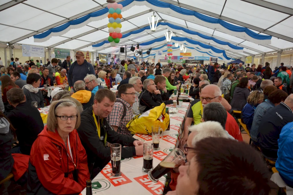 Gruppe von Menschen in einem Festzelt bei einer Veranstaltung, mit Tischen und bunten Dekorationen.