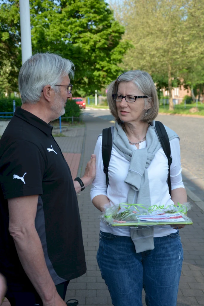 Älteres Paar im Gespräch auf Gehweg, sie hält ein Geschenk mit Schleife, bei sonnigem Wetter im Grünen.