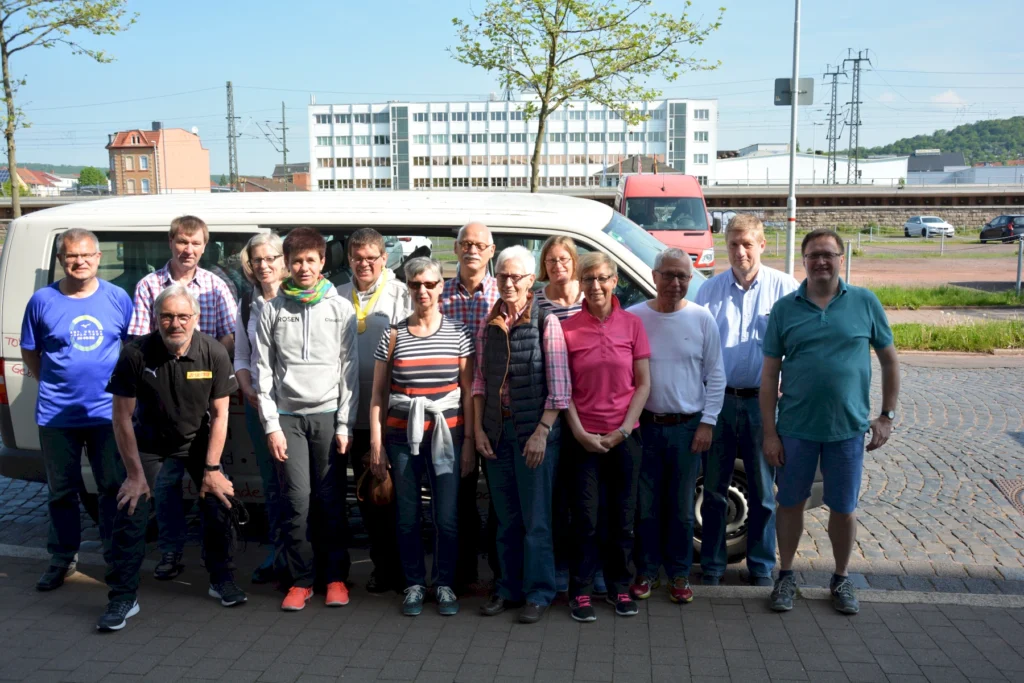 Gruppe von Menschen vor einem Minibus in urbaner Umgebung, sonniges Wetter, Freizeitkleidung.