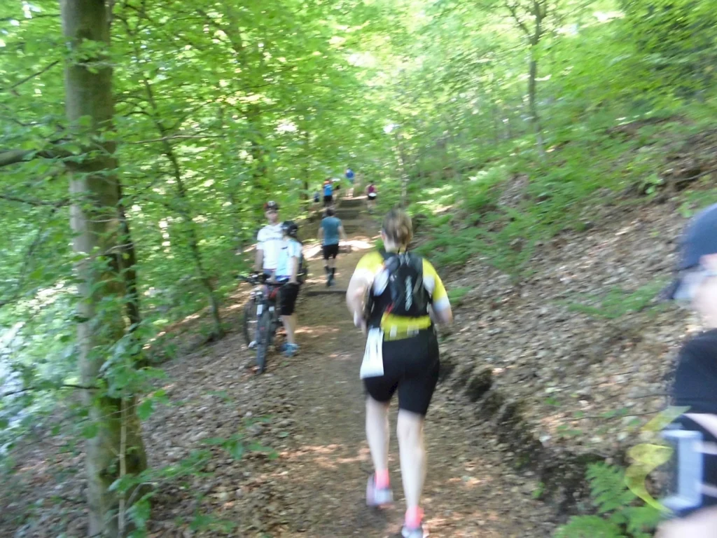 Läufer und Radfahrer auf einem schmalen Waldweg umgeben von üppigem Grün, während sie an einem Outdoor-Event teilnehmen.