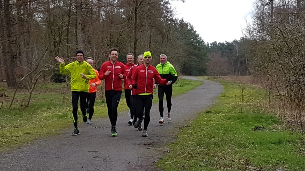 Gruppe von Joggern in bunter Sportkleidung joggt auf Waldweg an einem bewölkten Tag.