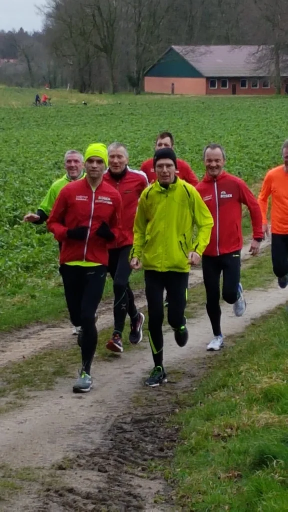 Gruppe von Läufern in bunter Sportkleidung beim Joggen auf einem Feldweg in einer ländlichen Umgebung.