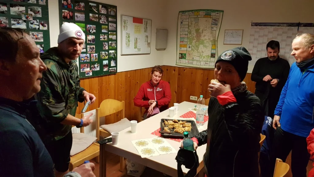 Gruppe von Personen in Sportkleidung genießt einen Snack in einem Raum mit Fotowand und Tisch voller Gebäck.