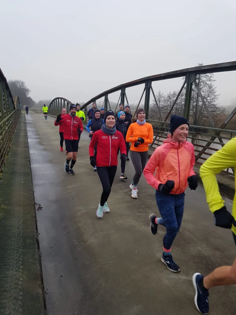 Gruppe von Läufern auf einer Brücke beim Joggen an einem nebligen Tag. Ideal für Ausdauer und Fitness.