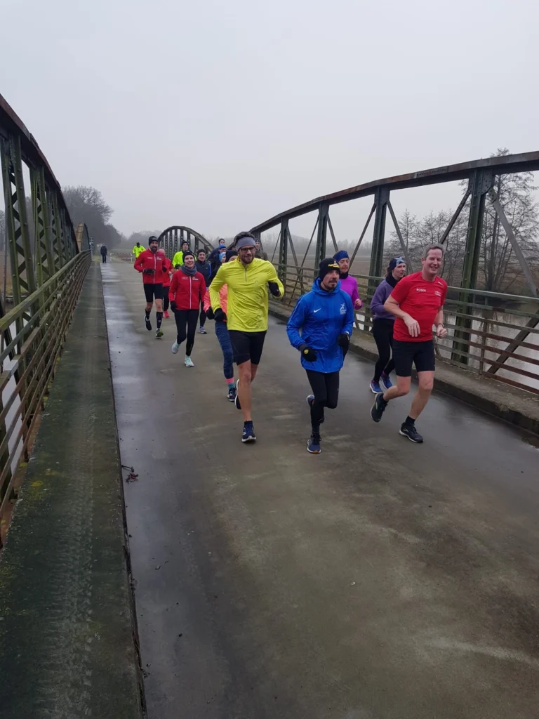 Gruppe von Menschen joggt auf einer Brücke an einem bewölkten Tag.