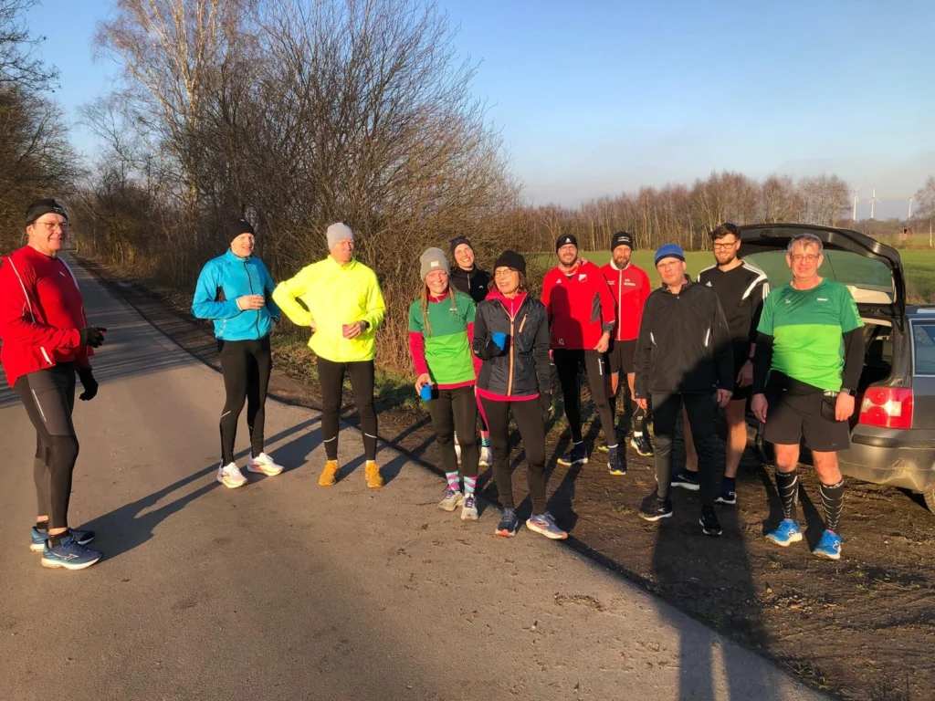 Gruppe von Läufern in bunter Sportkleidung auf einer Landstraße, bereit für das Training an einem sonnigen Tag.