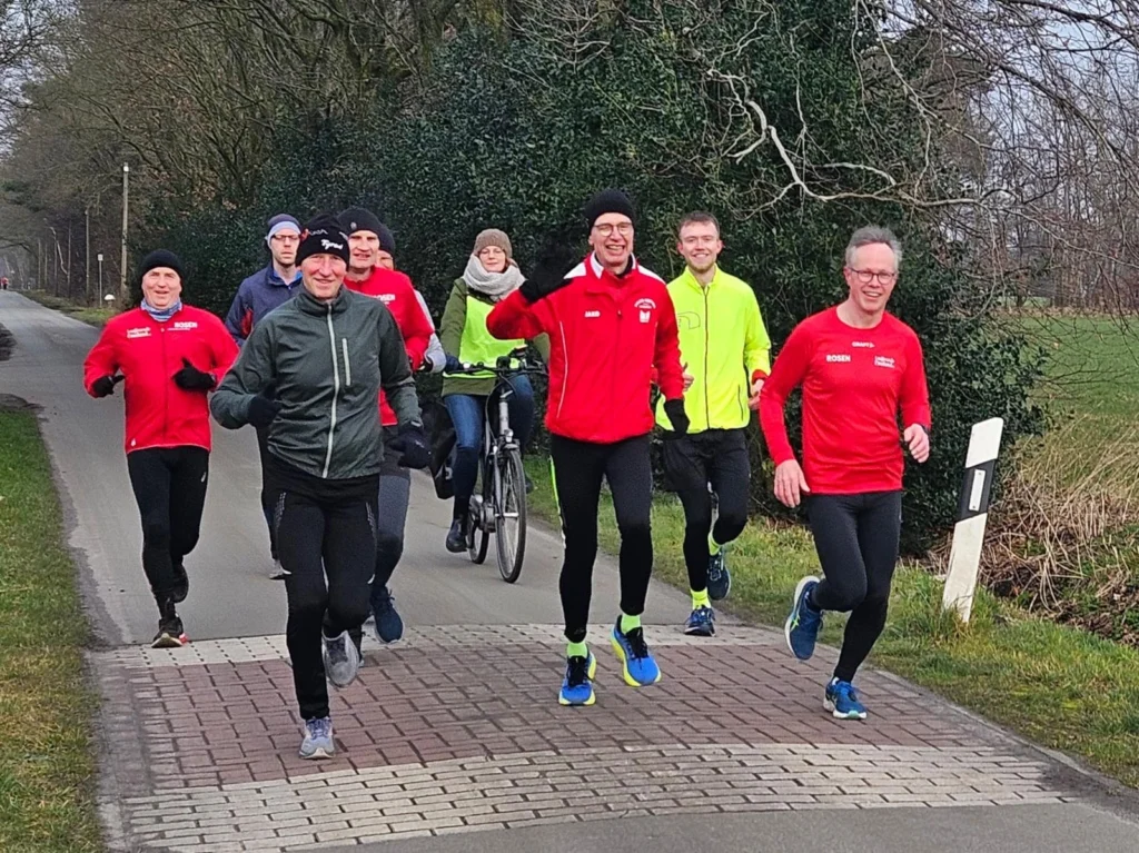 Gruppe von Läufern in bunter Sportkleidung joggt auf einer ländlichen Straße an einem Wintertag.