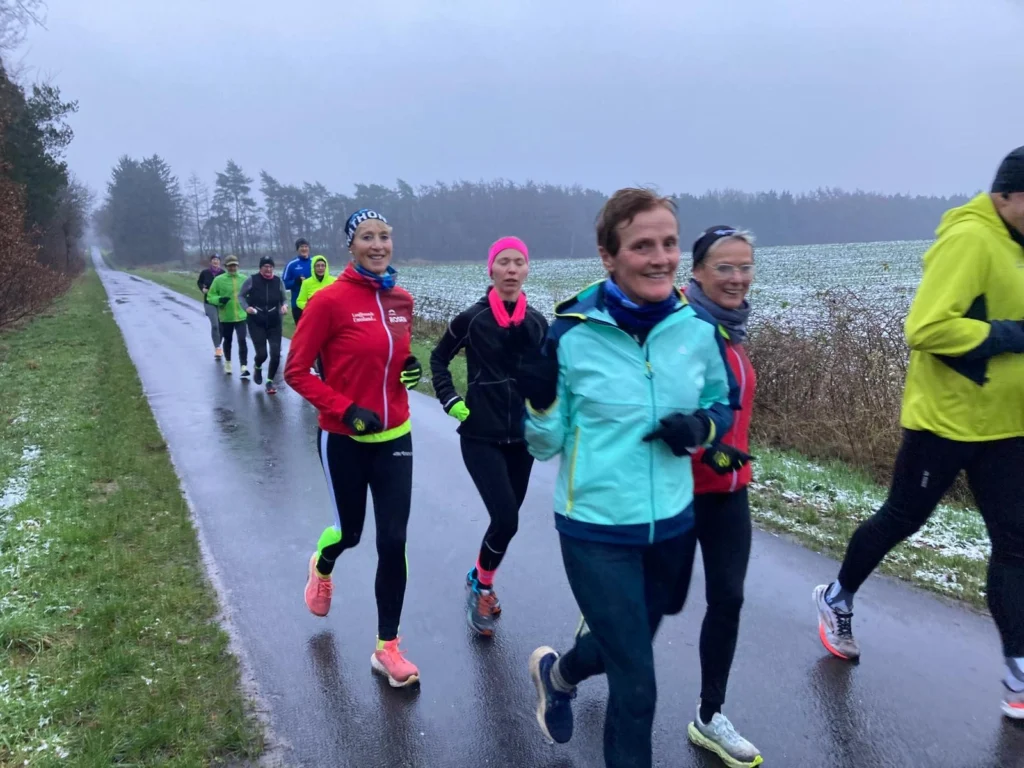 Gruppe von Läufern joggt an einem winterlichen, nassen Feldweg entlang, bedeckt mit leichter Schneeschicht.