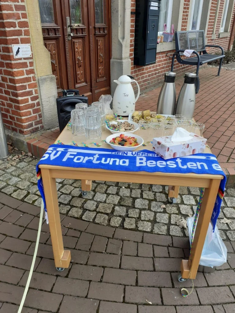Tee und Snacks auf einem Tisch vor einem Gebäude, dekoriert mit Fortuna Beesten Schal.