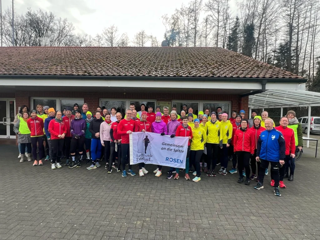 Gruppe von Läufern in bunter Sportkleidung posiert vor einem Gebäude mit einem Banner Gemeinsam an die Spitze.
