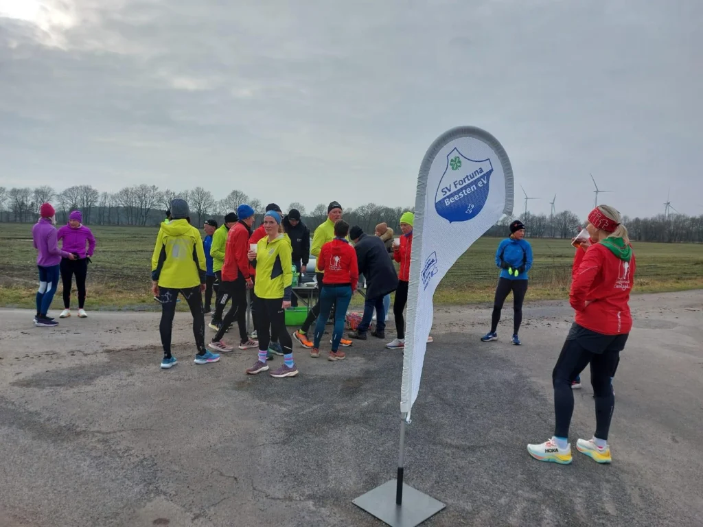 Läufergruppe im Freien bei einer Veranstaltung von SV Fortuna Beesten e.V., stehen am Straßenrand mit Fahne und Feldern.