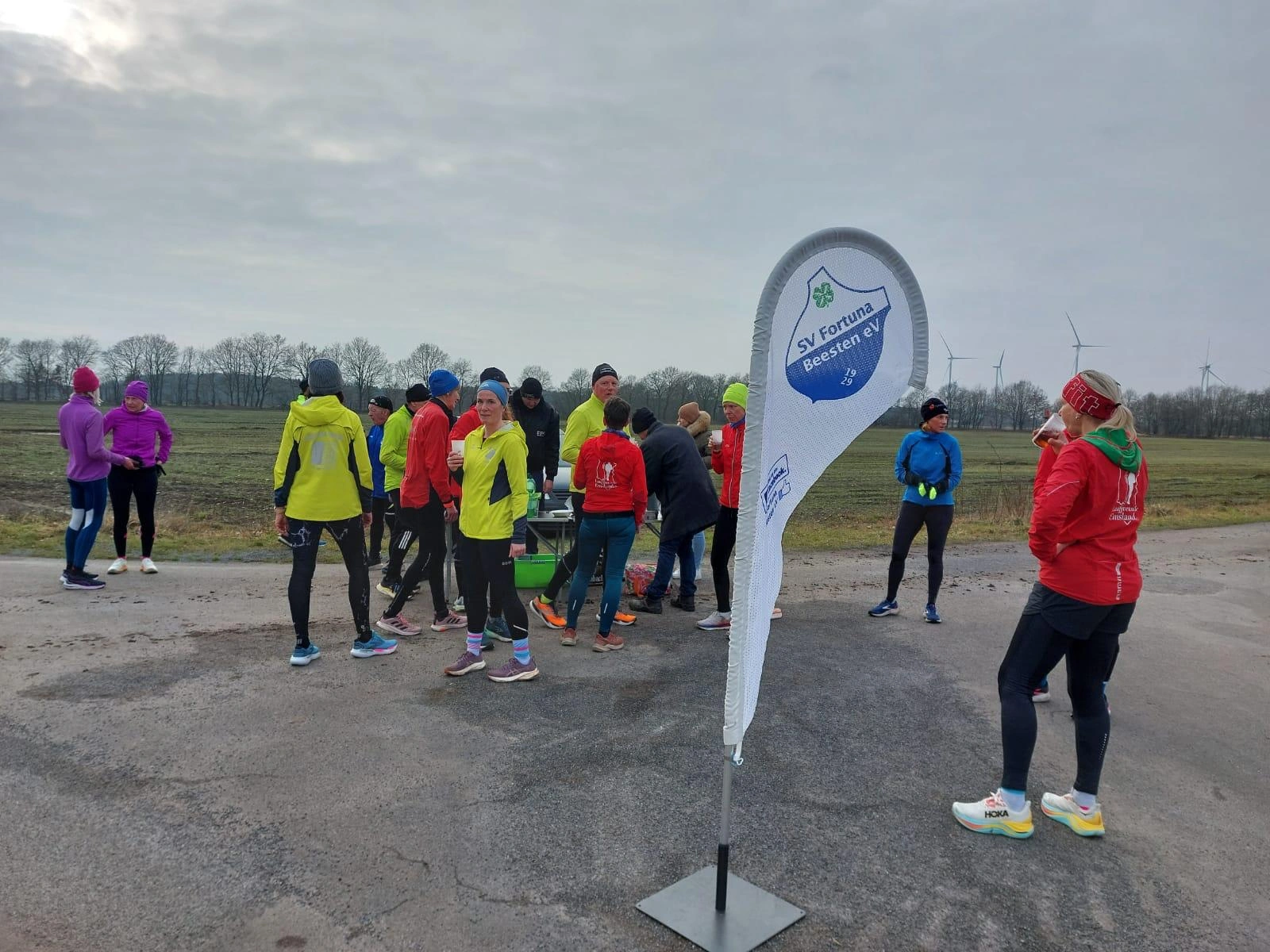 Läufergruppe im Freien bei einer Veranstaltung von SV Fortuna Beesten e.V., stehen am Straßenrand mit Fahne und Feldern.