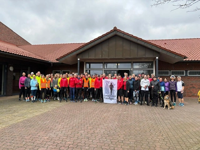 Gruppe von Läufern vor einem Gebäude, einige halten ein Banner, Sportveranstaltung im Freien, bewölkter Himmel.