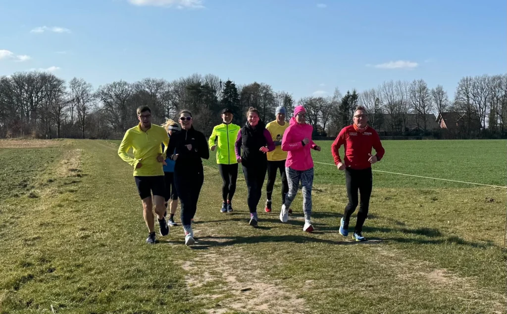 Gruppe von Menschen joggt auf einem Feldweg bei sonnigem Wetter, umgeben von Bäumen. Fitness und Natur.