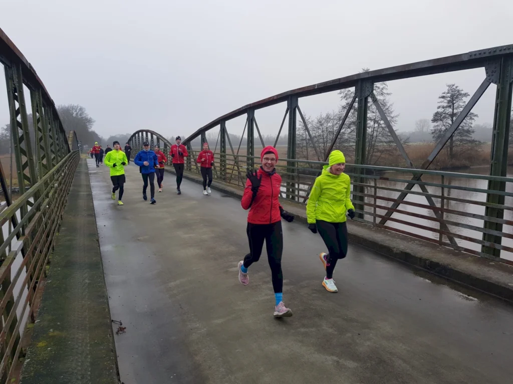 Gruppe von Läufern auf Brücke bei bewölktem Wetter, trägt bunte Sportbekleidung, motiviert und energisch.