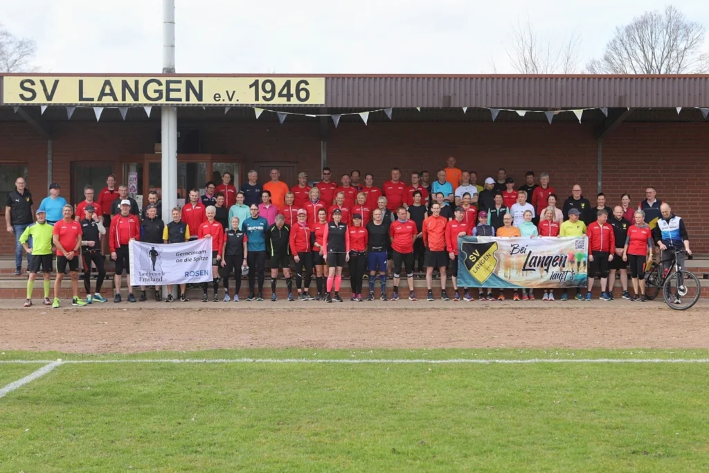 Gruppenfoto des SV Langen e.V. 1946 mit Mitgliedern und Trainern in Sportbekleidung, die vor dem Vereinsgebäude stehen. Einige halten Banner mit der Aufschrift "Gemeinsam an die Spitze" und "Bei Langen läuft's". Die Veranstaltung zeigt die Gemeinschaft und den Teamgeist des Vereins.