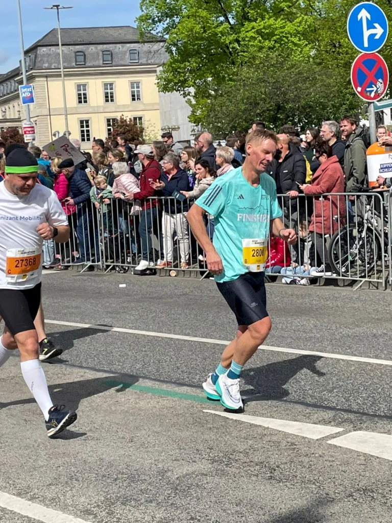 Läufer beim Marathon mit der Startnummer 2800, umgeben von Zuschauern, die an der Strecke stehen. Im Hintergrund Gebäude und Bäume, sonniger Tag.