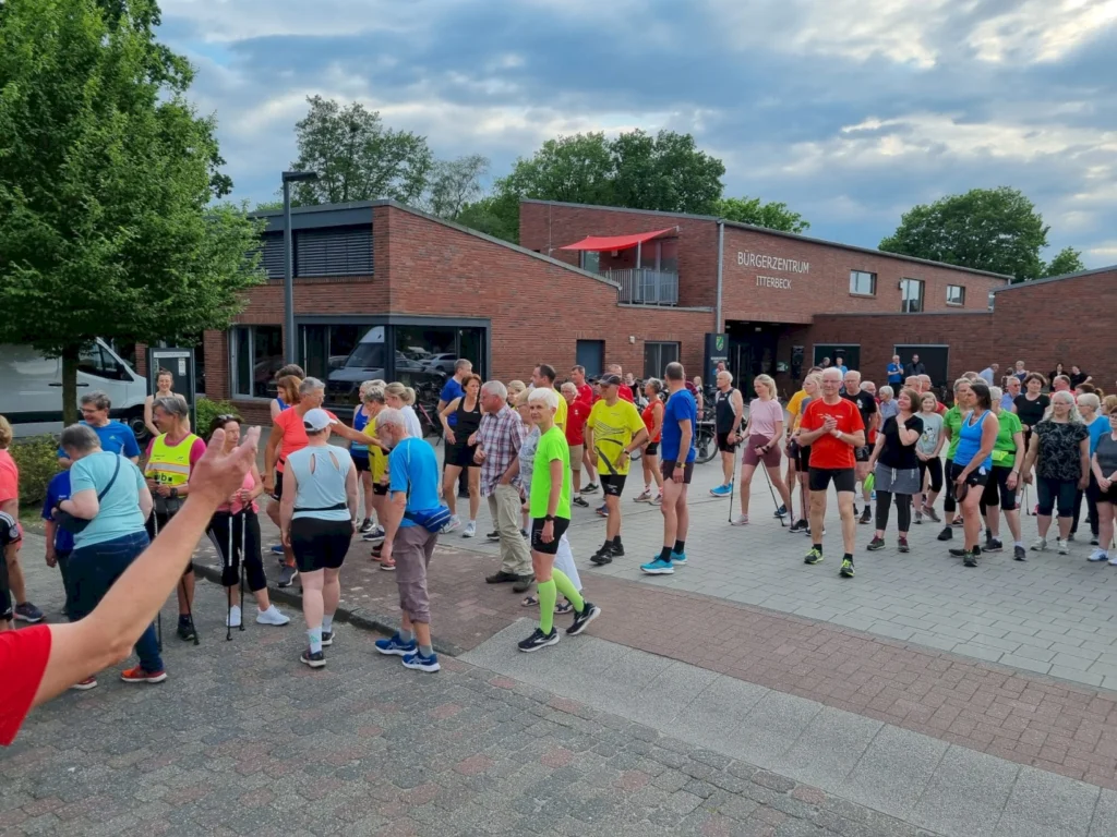 Viele Teilnehmer versammeln sich vor dem Bürgerzentrum in Itterbeck für eine Sportveranstaltung, während einige bereits in sportlicher Kleidung sind. Die Gruppe besteht aus Männern und Frauen unterschiedlichen Alters, die sich auf den Beginn der Veranstaltung vorbereiten.