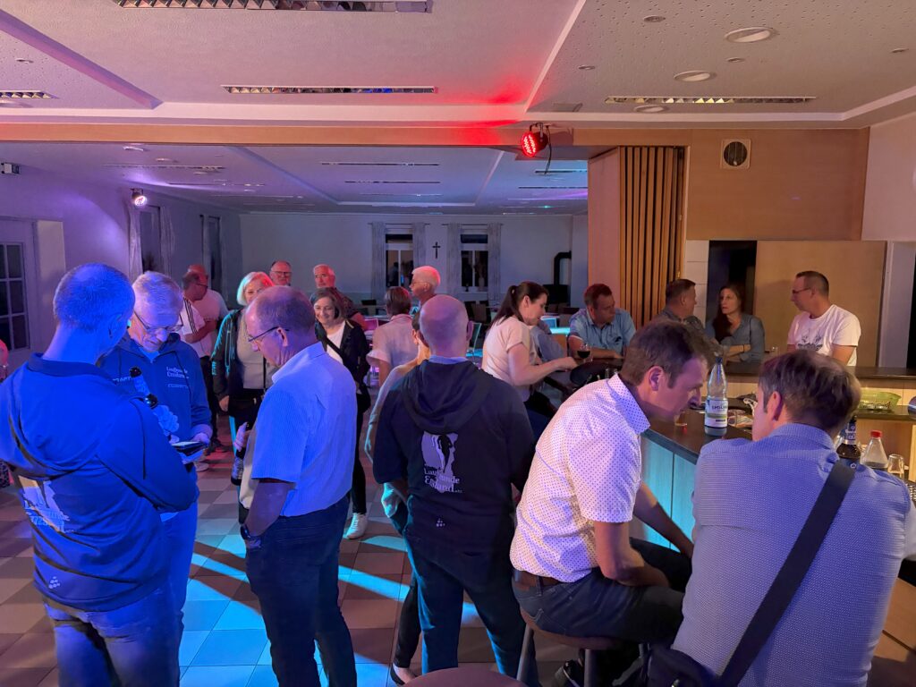 Menschen unterhalten sich bei einer geselligen Veranstaltung in einem Raum mit Bar und bunter Beleuchtung.