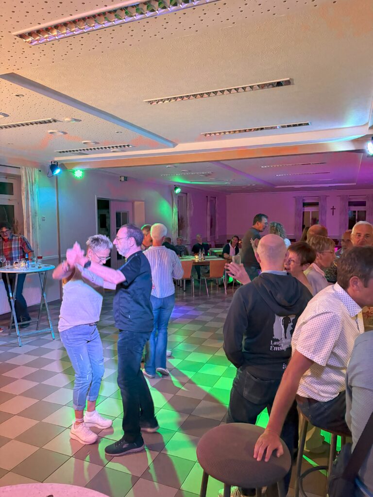 Menschen tanzen fröhlich in einem beleuchteten Raum bei einer Feier oder Party mit buntem Licht.