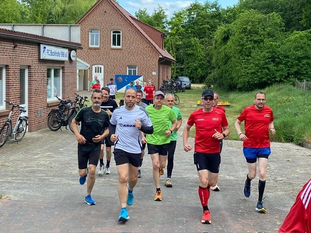 Gruppe von Läufern in Sportkleidung joggt auf gepflastertem Weg vor einem Backsteingebäude, umgeben von Bäumen.